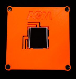 An orange, 3D-printed test part fixture holds a small cylinder optic